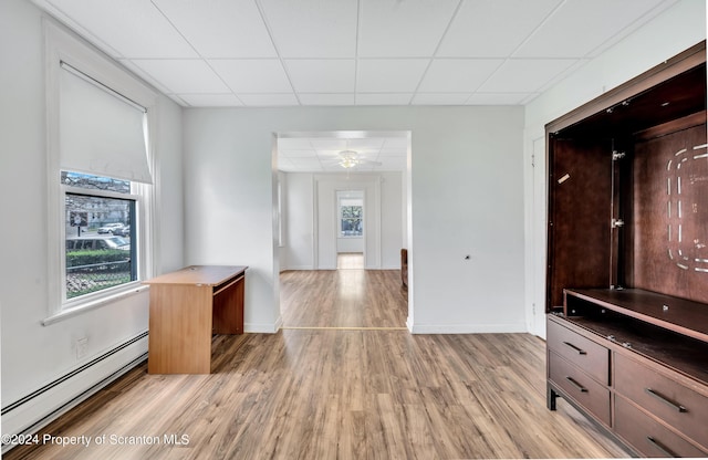 unfurnished living room with light wood-type flooring, a drop ceiling, a baseboard heating unit, and ceiling fan