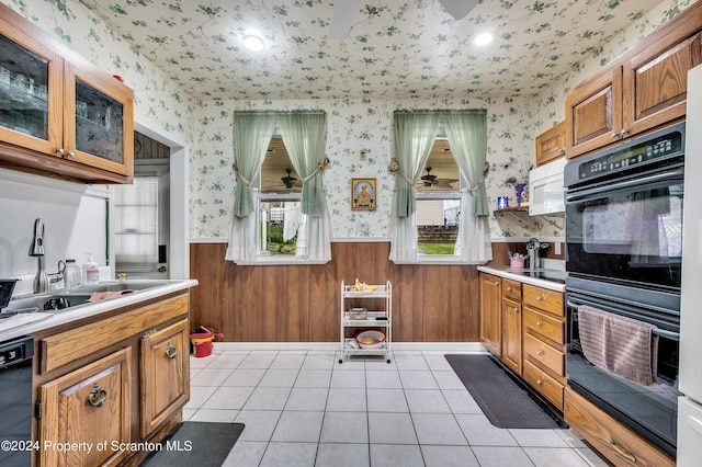 kitchen with black appliances, light tile patterned flooring, wood walls, and sink