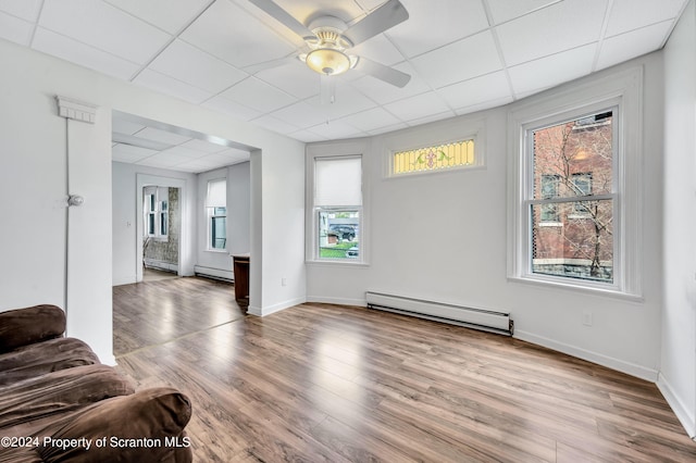 living room featuring baseboard heating, a drop ceiling, and plenty of natural light