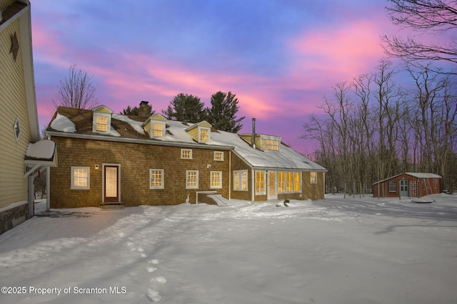 snow covered back of property featuring a storage shed