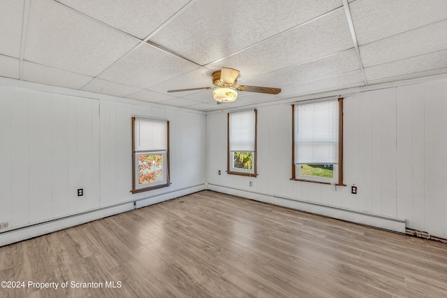 spare room with light wood-type flooring, a drop ceiling, wood walls, and ceiling fan