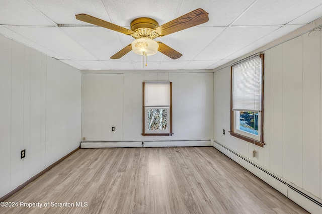 spare room with wooden walls, light hardwood / wood-style floors, a drop ceiling, and a baseboard heating unit