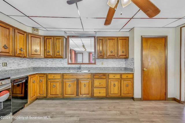 kitchen featuring light stone countertops, sink, a drop ceiling, black dishwasher, and light wood-type flooring