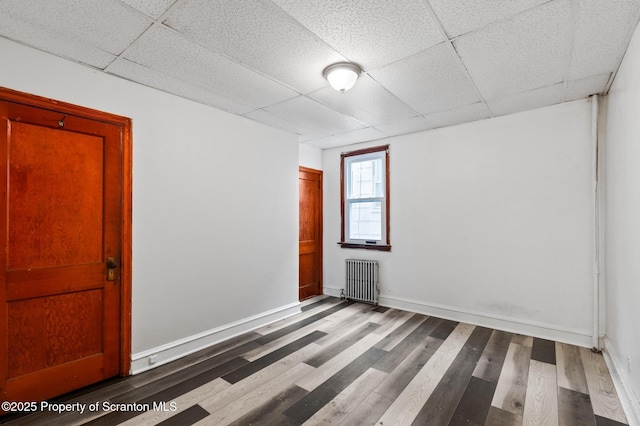spare room with dark wood-type flooring, baseboards, a paneled ceiling, and radiator heating unit