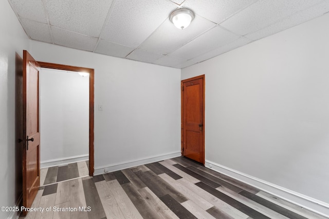empty room featuring dark wood-type flooring, baseboards, and a drop ceiling