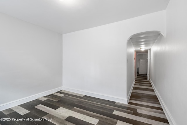 unfurnished room with arched walkways, baseboards, and dark wood-style floors