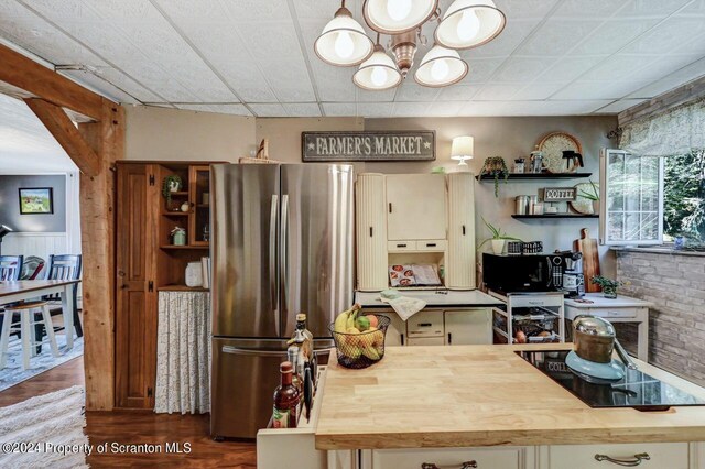 kitchen with wood counters, stainless steel fridge, brick wall, wood-type flooring, and an inviting chandelier