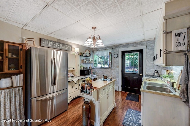 kitchen with pendant lighting, wood counters, white cabinets, sink, and stainless steel fridge