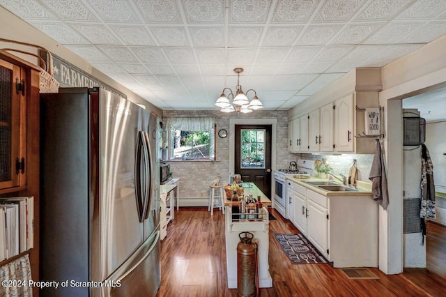 kitchen featuring white cabinets, sink, white range with gas stovetop, stainless steel refrigerator, and hanging light fixtures