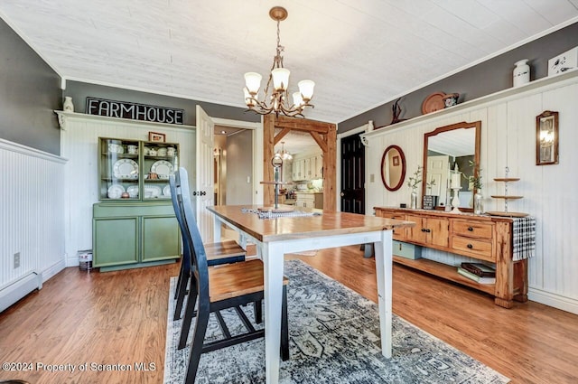 dining area with a baseboard radiator, an inviting chandelier, wood-type flooring, wooden walls, and ornamental molding