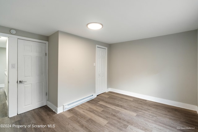 unfurnished bedroom with baseboard heating, a closet, and hardwood / wood-style flooring