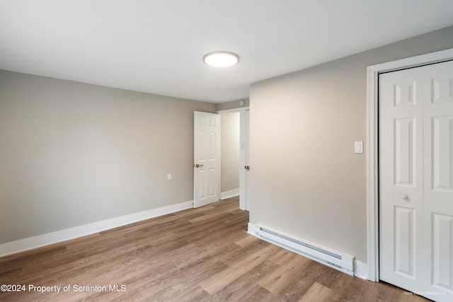 unfurnished bedroom featuring a closet, baseboard heating, and light hardwood / wood-style floors