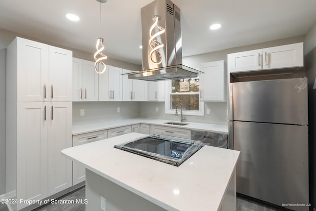 kitchen with white cabinets, hanging light fixtures, sink, island range hood, and stainless steel refrigerator