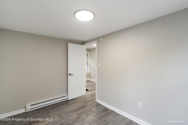 spare room featuring baseboard heating and dark wood-type flooring