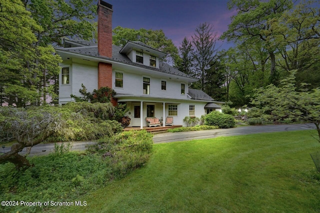 back house at dusk featuring a lawn and a porch