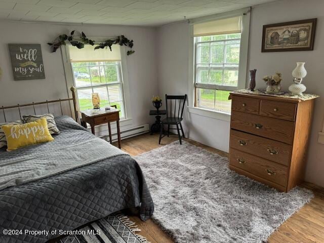 bedroom with light wood-type flooring, multiple windows, and a baseboard radiator