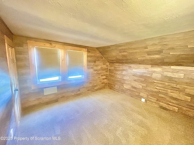 bonus room with wooden walls, visible vents, vaulted ceiling, and a textured ceiling