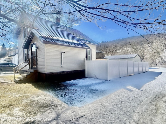 view of side of home featuring entry steps, a standing seam roof, fence, and metal roof