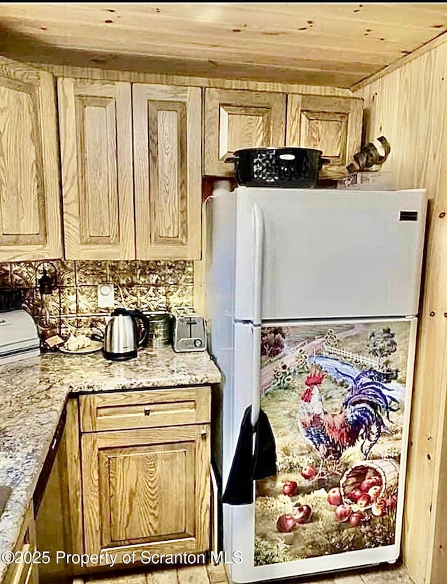 kitchen with wood ceiling, light stone counters, freestanding refrigerator, and wooden walls