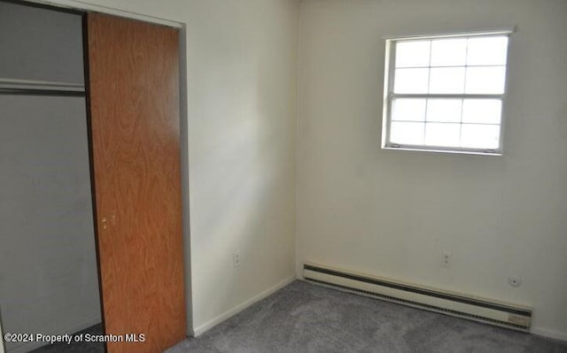 unfurnished bedroom with carpet, a closet, and a baseboard heating unit