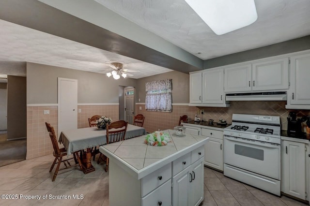 1130 Stafford Ave, Scranton, PA 18504 - kitchen featuring white range with gas stovetop, under cabinet range hood, tile countertops, tile walls, and light tile patterned flooring