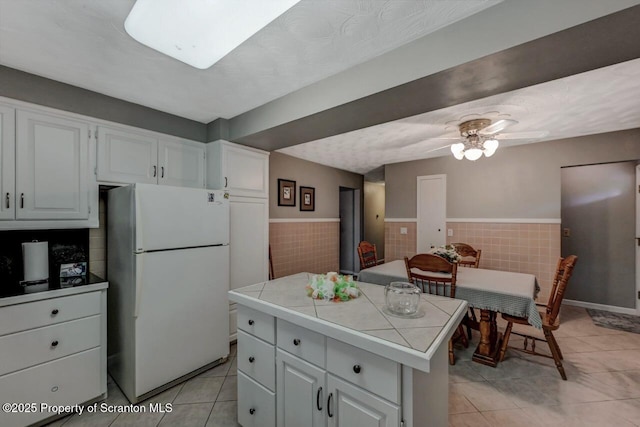 1130 Stafford Ave, Scranton, PA 18504 - kitchen featuring freestanding refrigerator, tile countertops, light tile patterned floors, white cabinets, and wainscoting