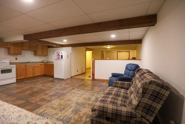 kitchen with a drop ceiling, open floor plan, white appliances, light countertops, and baseboards