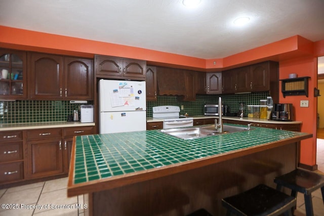 kitchen featuring backsplash, dark brown cabinetry, a kitchen bar, light tile patterned flooring, and white appliances