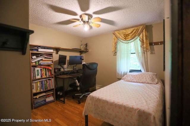 bedroom with a textured ceiling, baseboard heating, wood finished floors, and a ceiling fan