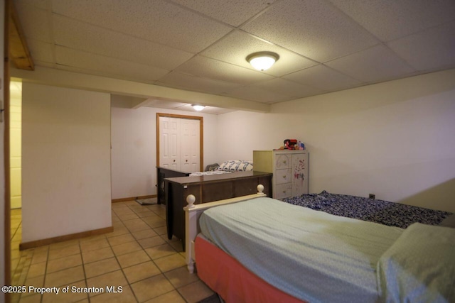 bedroom with a drop ceiling, baseboards, and light tile patterned flooring