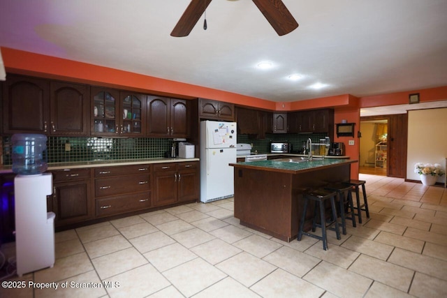 kitchen featuring white appliances, a ceiling fan, a breakfast bar, decorative backsplash, and dark brown cabinets