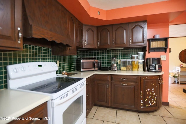 kitchen with stainless steel microwave, backsplash, light countertops, light tile patterned floors, and white range with electric stovetop