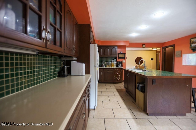 kitchen featuring backsplash, dark brown cabinets, glass insert cabinets, freestanding refrigerator, and a sink