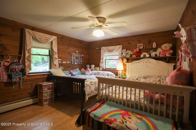 bedroom featuring multiple windows, a baseboard heating unit, wood walls, and wood finished floors