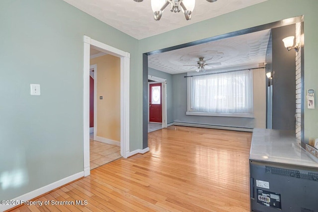 unfurnished dining area featuring a baseboard radiator, ceiling fan with notable chandelier, light hardwood / wood-style flooring, and a textured ceiling