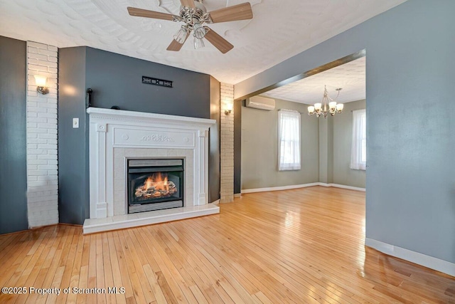 unfurnished living room featuring a tiled fireplace, ceiling fan, a wall mounted AC, and light hardwood / wood-style floors