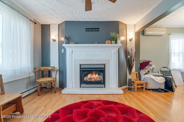 living area with hardwood / wood-style flooring, ceiling fan, a wall mounted air conditioner, and a fireplace