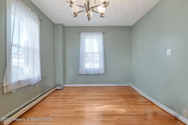 empty room featuring a baseboard heating unit, a notable chandelier, and light wood-type flooring