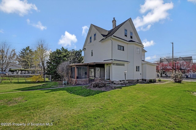 rear view of property featuring a chimney, a sunroom, and a yard