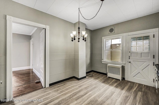 unfurnished dining area featuring hardwood / wood-style flooring, radiator, and a notable chandelier