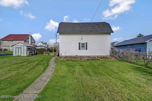 exterior space with fence, a yard, an outdoor structure, a storage unit, and roof with shingles