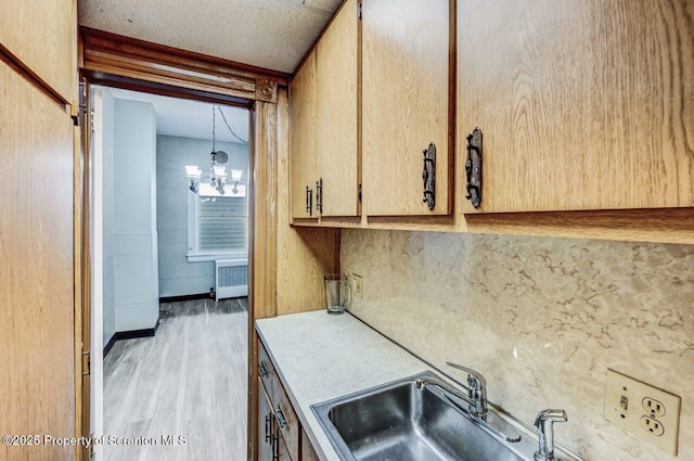 kitchen with radiator, sink, an inviting chandelier, hanging light fixtures, and light hardwood / wood-style floors