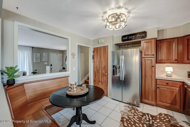 kitchen with light tile patterned floors, stainless steel fridge with ice dispenser, light countertops, and brown cabinets