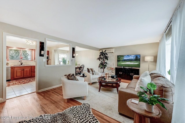 living room featuring a wall mounted air conditioner, a notable chandelier, and light wood-style floors