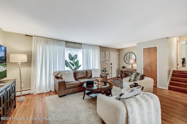 living area featuring stairway, a baseboard radiator, light wood-style flooring, and baseboards