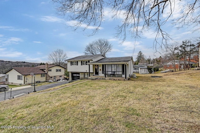 tri-level home with aphalt driveway, a residential view, a front yard, a porch, and a garage