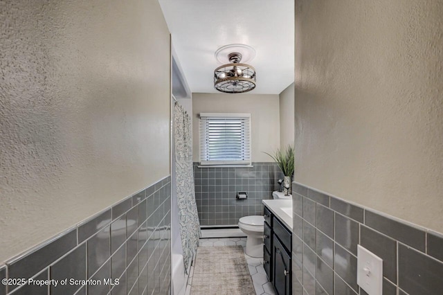 bathroom featuring tile patterned flooring, wainscoting, tile walls, toilet, and curtained shower