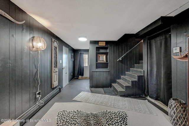 entryway featuring wooden walls, stairs, and finished concrete floors