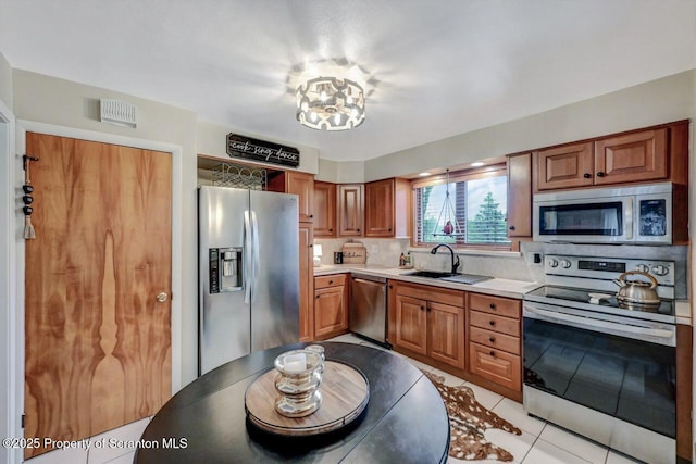 kitchen featuring light tile patterned floors, a sink, appliances with stainless steel finishes, light countertops, and brown cabinetry