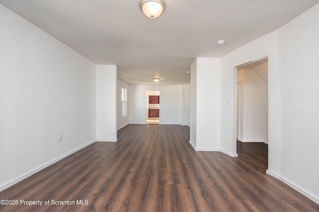 empty room with baseboards and dark wood-type flooring